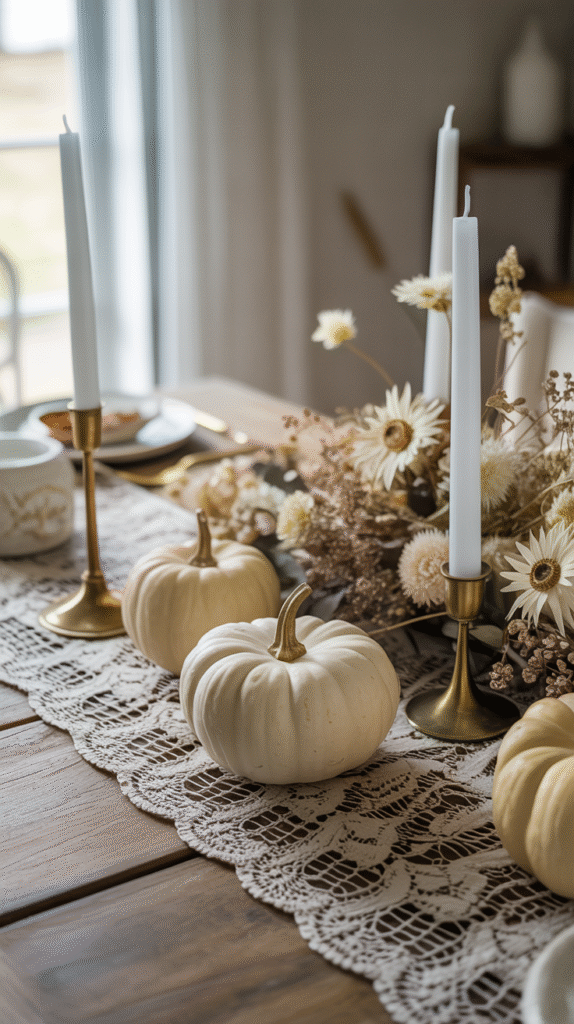 Elegant fall table decor with white pumpkins, lace runner, brass candle holders, and dried flowers.